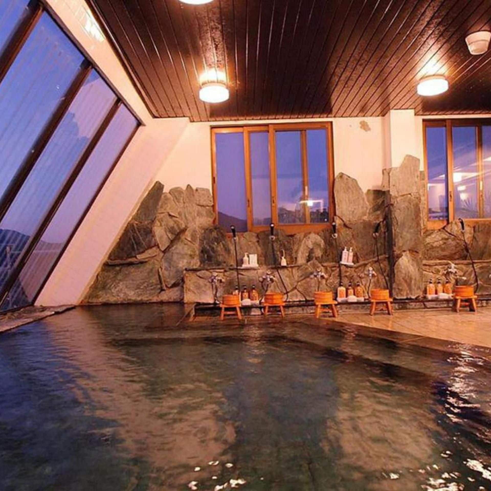 Piscina interna com teto de madeira e paredes de pedra, bancos e garrafas.