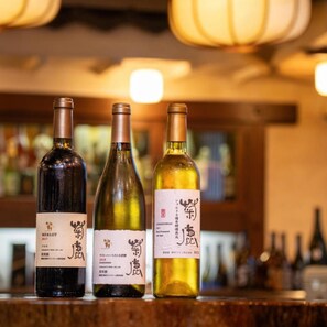 Three bottles of wine on a bar counter with a blurred background of other bottles.