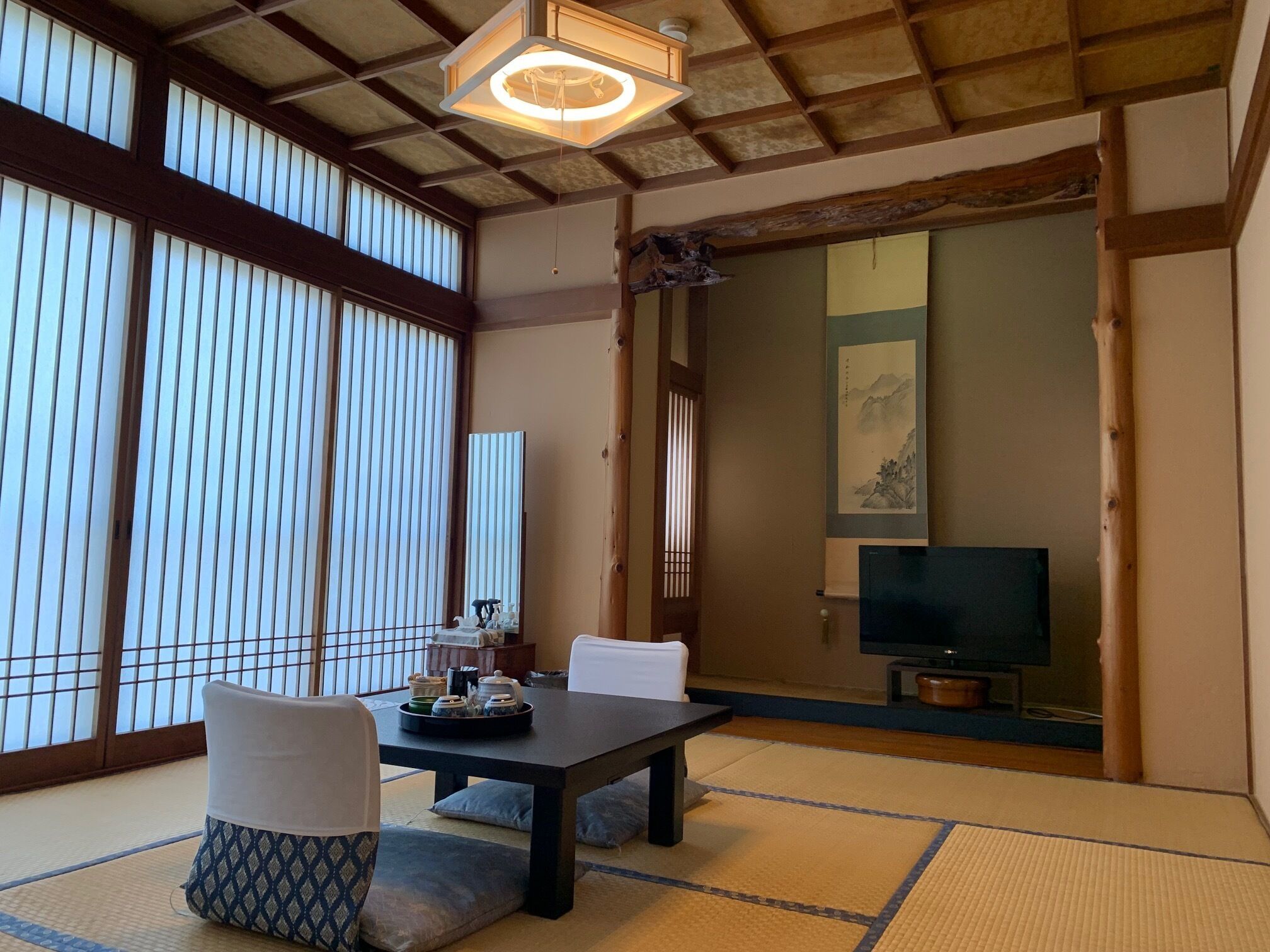 Een traditionele Japanse kamer met tatami vloerbedekking, een lage tafel en een televisie op de achtergrond.