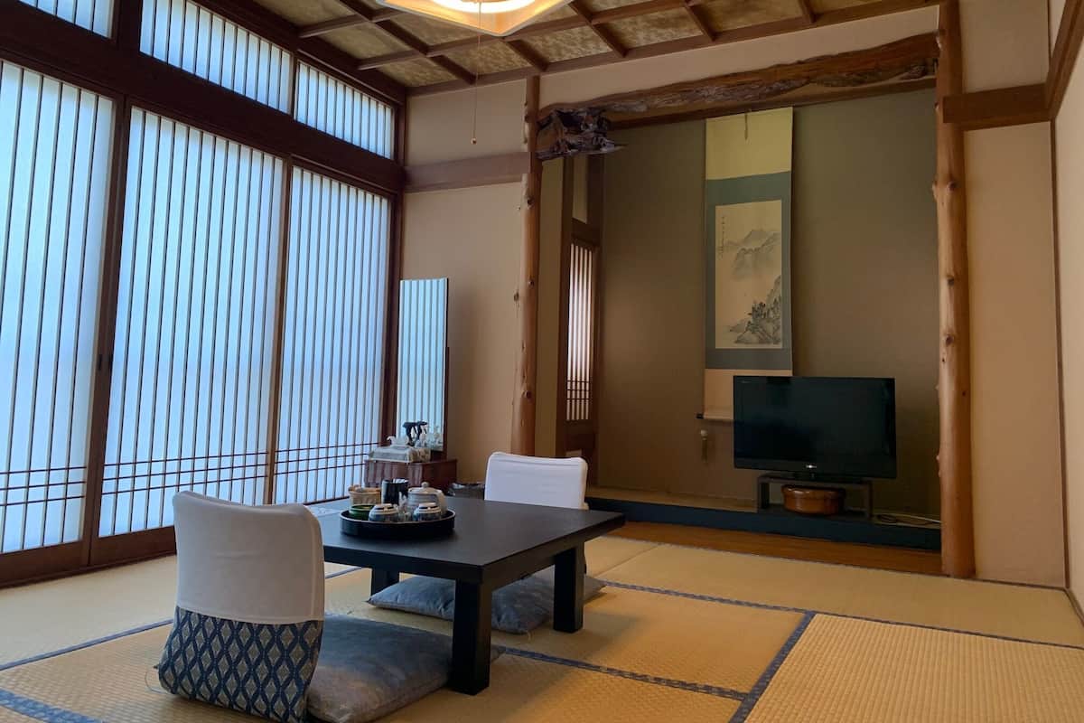 A traditional Japanese room with tatami flooring, a low table, and a television in the background.