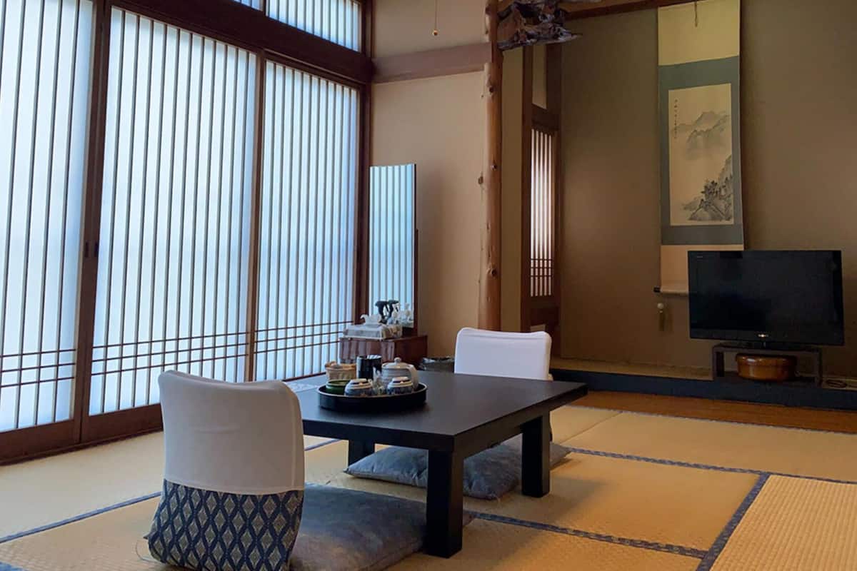 A traditional Japanese-style room with tatami flooring, a low table, white chairs, and a television.