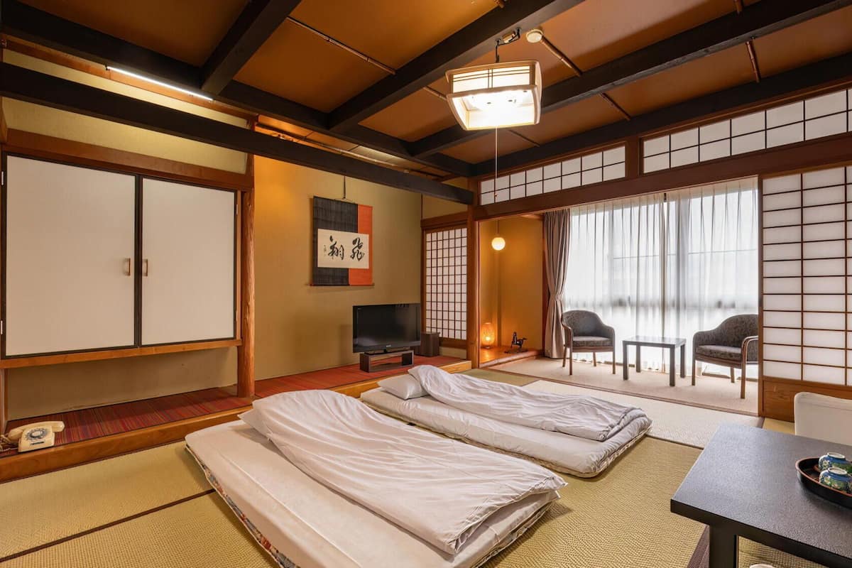 A traditional Japanese-style room with tatami flooring, a futon bed, a television, and sliding doors with shoji screens.