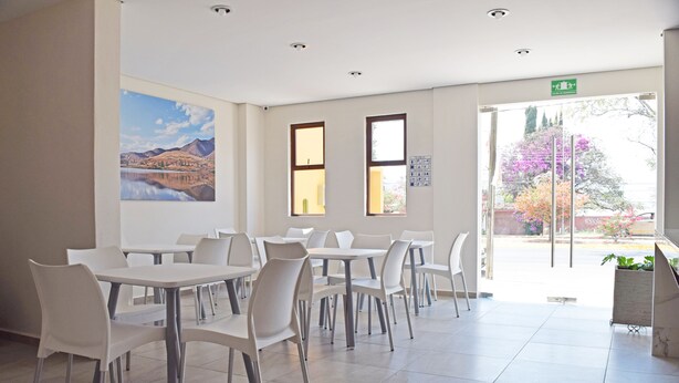 Un vaste espace de restauration intérieur, avec des tables et des chaises blanches, de grandes fenêtres et un tableau accroché au mur.