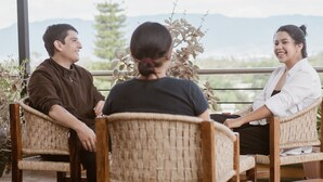 Trois personnes sont assises sur des chaises en osier, à l'extérieur, avec une vue sur les montagnes en arrière-plan.