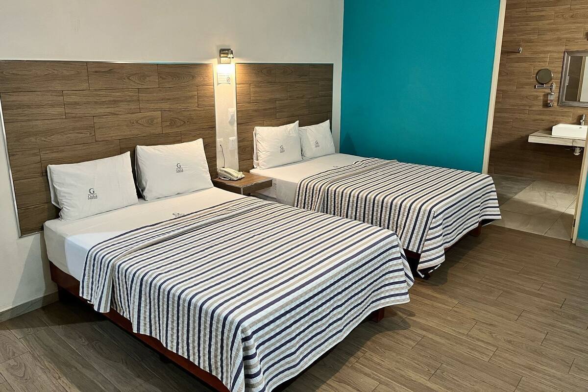 A hotel room with two beds, a nightstand, a wall-mounted light, and a bathroom with a sink and mirror.