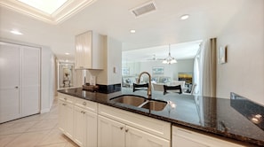 A modern kitchen with a large island, stainless steel sink, and white cabinetry.