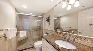 A modern bathroom with a glass-enclosed shower, a sink with a granite countertop, and a large mirror. - House Of The Sun #501GS (Sarasota)