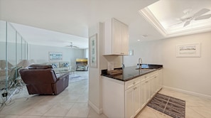 A modern kitchen with white cabinets, a black countertop, and a ceiling fan. - House Of The Sun #501GS (Sarasota)