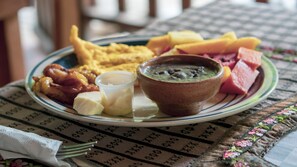 Un plato de comida con huevos, tocino, jamón y un tazón de sopa sobre una mesa con mantel estampado.
