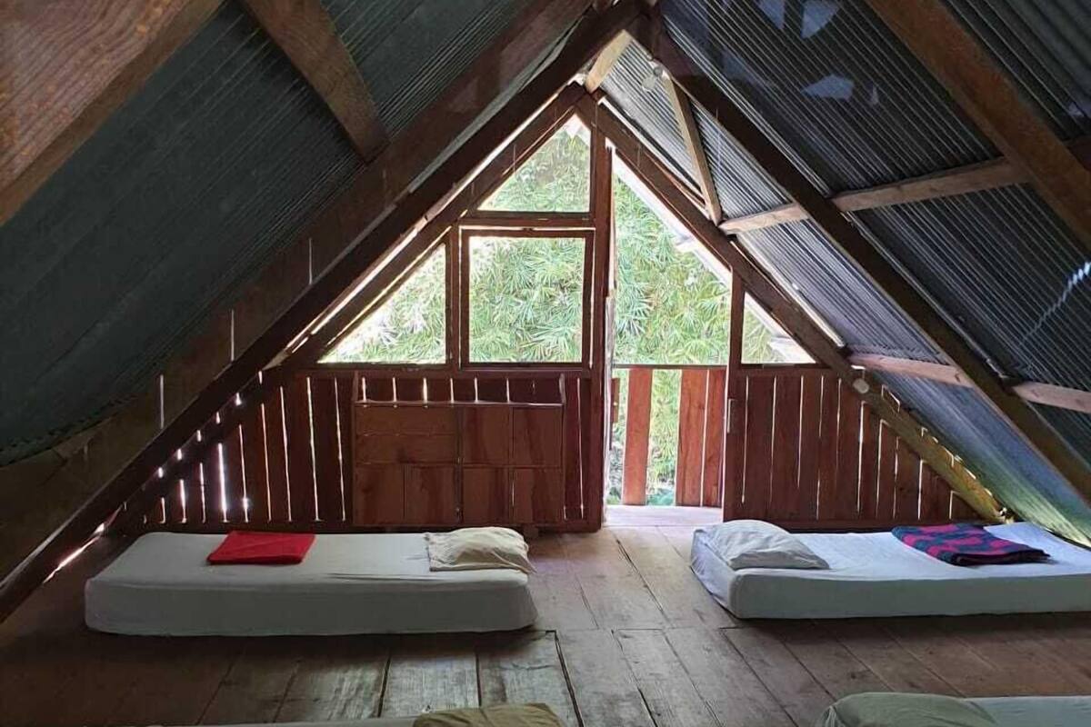 A cozy attic bedroom with wooden floors, sloped ceilings, and large windows.