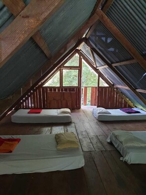 Un dormitorio acogedor en el ático, con pisos de madera, techos inclinados y ventanas grandes.