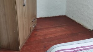 Ein Schlafzimmer mit einem Holzschrank, einem Bett mit gestreifter Bettdecke und einer weißen Wand mit einer Holzablage.