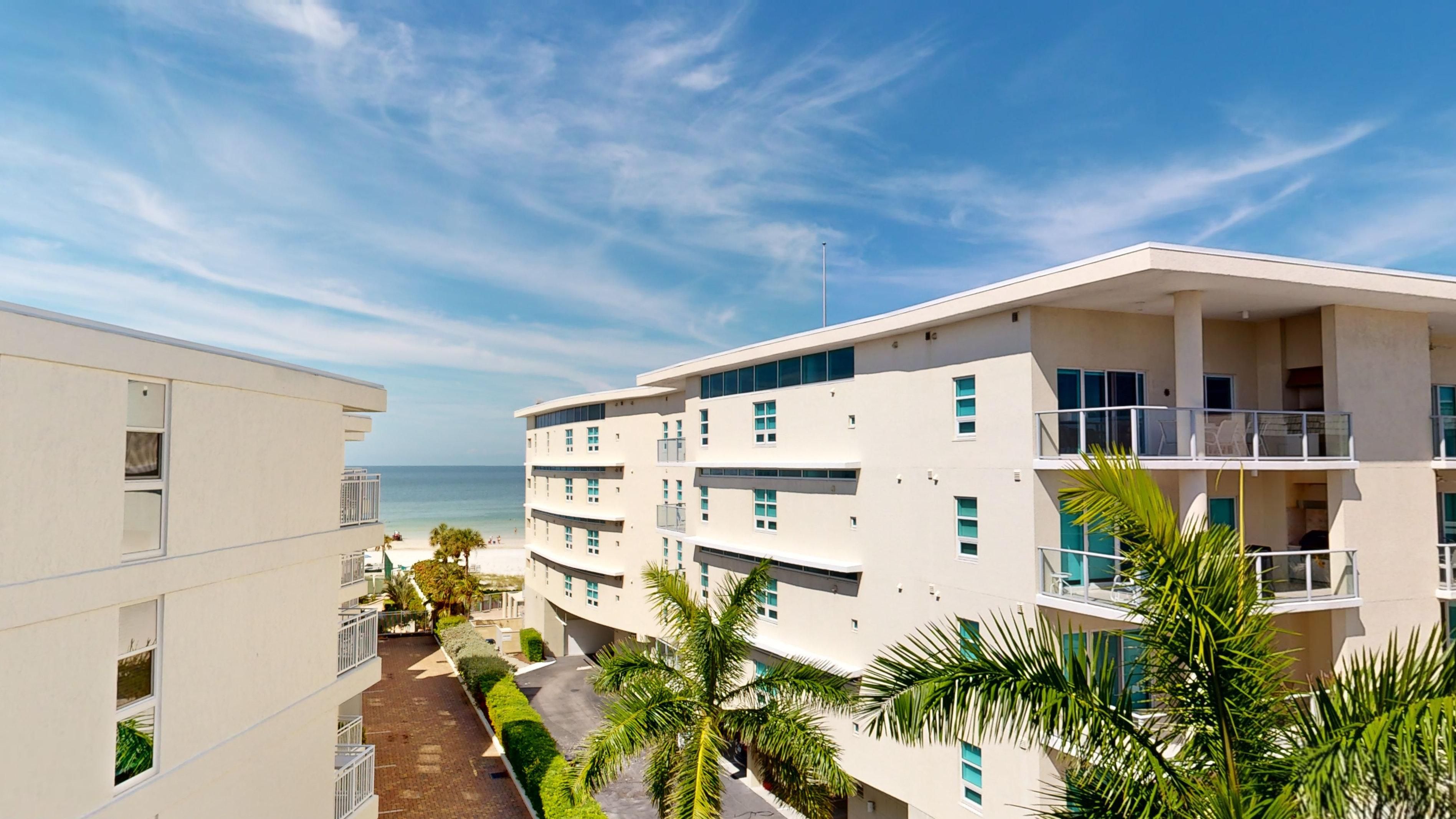 Un hôtel à plusieurs étages doté de balcons donnant sur une plage, un ciel dégagé et des palmiers.
