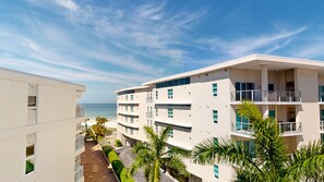 Ein mehrstöckiges Hotel mit Balkonen mit Blick auf einen Strand, einem klaren Himmel und Palmen.