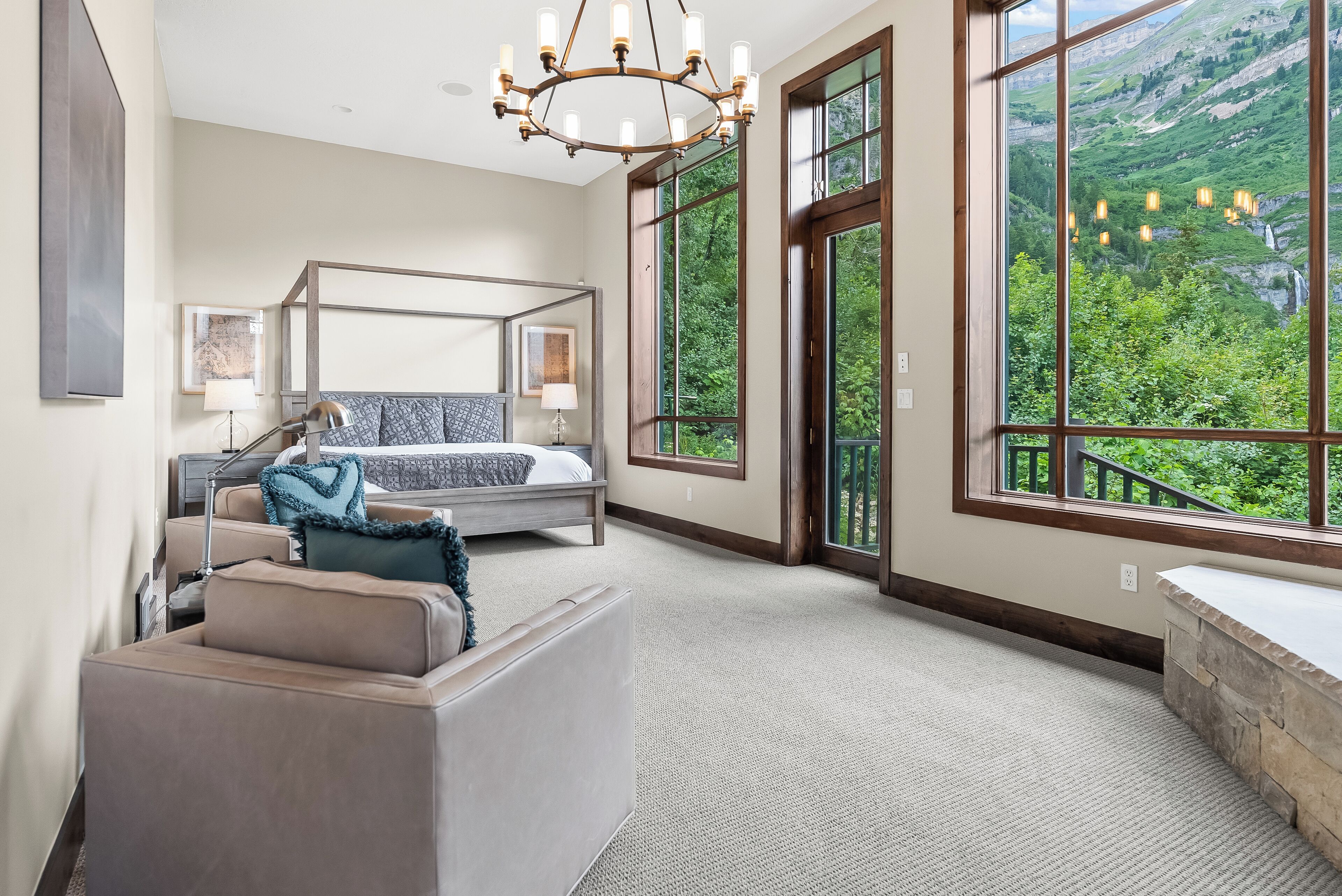 A modern bedroom with a large window, a bed, a seating area, and a chandelier.