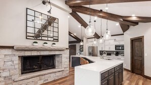 A modern kitchen with a stone fireplace, wooden beams, and pendant lighting. - Mountain Lodge Overlooking Waterfall - Hot Tub, 5 bedroom, Unbelievable Views! (Sundance)