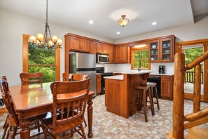 A modern kitchen with wooden cabinets, a central island, and a dining area with wooden chairs. - Hide'n Go Creek-Waterfront, Hot tub, firepit (Ellijay)