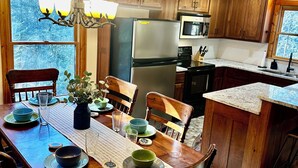 Una cucina con mobili in legno, un frigorifero, un forno a microonde e un tavolo da pranzo apparecchiato con sedie e piatti.