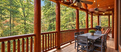 A wooden deck with a table and chairs, surrounded by a railing, overlooking a forested area.
