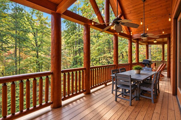 A wooden deck with a table and chairs, surrounded by a railing, overlooking a forested area.