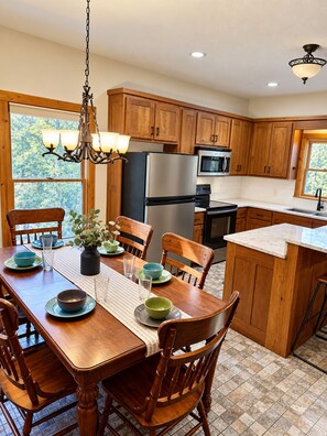 A kitchen with wooden cabinets, a stainless steel refrigerator, a microwave, and a dining area with a wooden table and chairs. - Hide'n Go Creek-Waterfront, Hot tub, firepit (Ellijay)