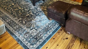 Un soggiorno accogliente con pavimento in legno, un tappeto decorato, un divano in pelle marrone e una scala in legno.