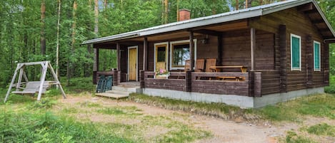 Maalaishenkinen mökki, jossa on kuisti, puinen ulkoverhous ja mökille johtava sorapolku.