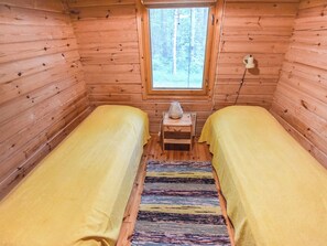 Una habitación tipo cabaña con dos camas, una ventana y una mesita con lámpara.