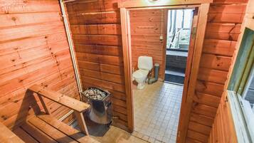 A wooden cabin interior with a wooden staircase, a small kitchen area with a stove, and a toilet visible through an open doorway.