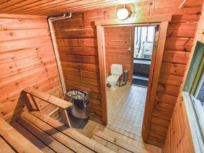 Een houten hutterend interieur met een houten trap, een klein keukentje met een fornuis en een toilet zichtbaar door een open deur.