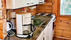 A compact kitchen with white cabinets, a coffee maker, a microwave, and a stove. - Mäntyranta by Interhome (Savonlinna)