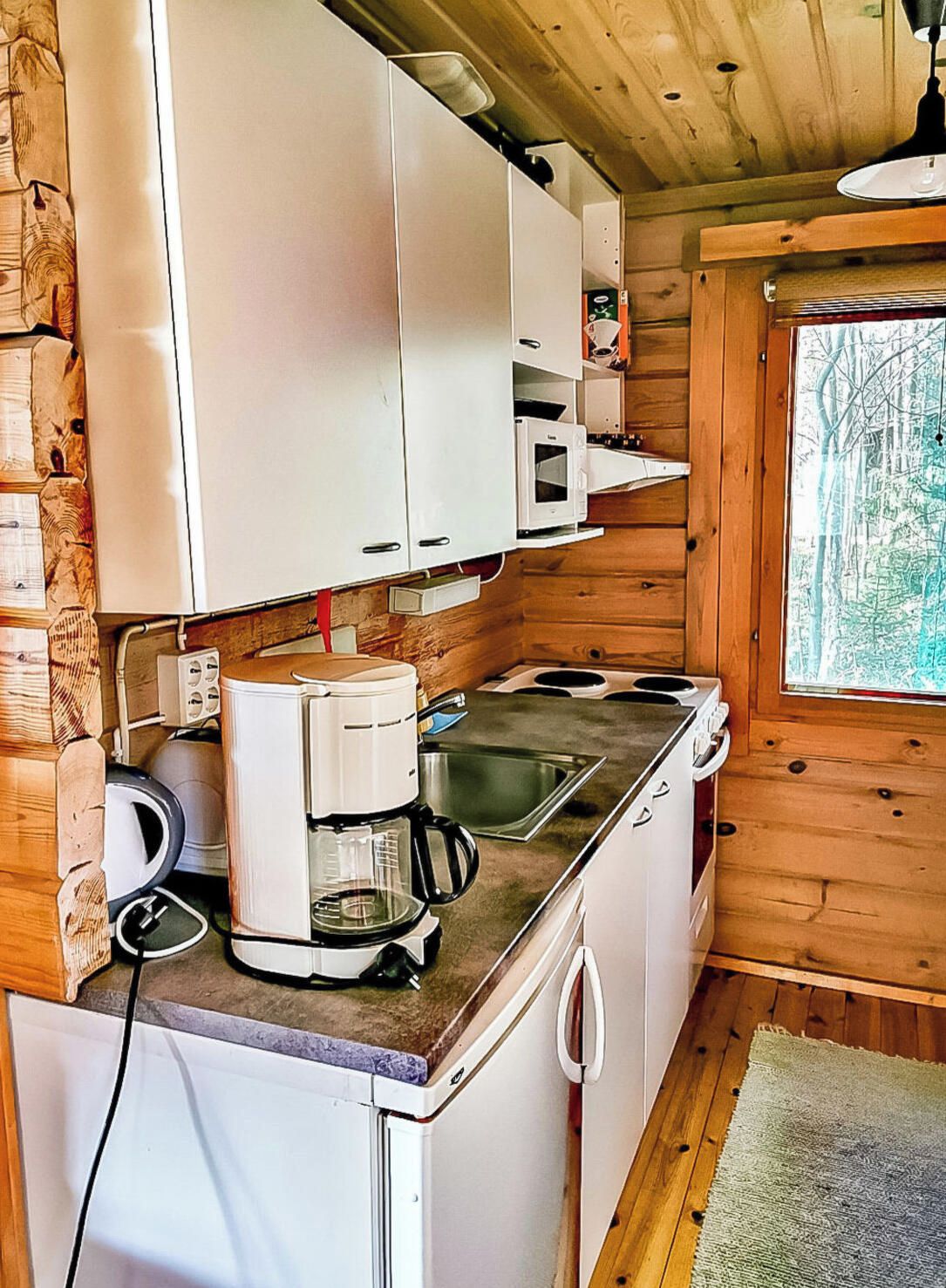 Pieni, käytännöllinen keittiö, jossa on valkoiset kaapit, kahvinkeitin, mikroaaltouuni ja pesuallas.