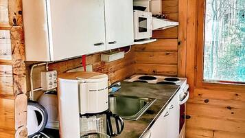 Pieni, käytännöllinen keittiö, jossa on valkoiset kaapit, kahvinkeitin, mikroaaltouuni ja pesuallas.
