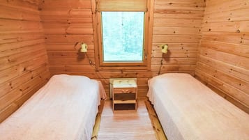 Pieni, viihtyisä mökkihuone, jossa on kaksi erillistä sänkyä, pieni puinen yöpöytä ja ikkuna, josta avautuu näkymä metsään.