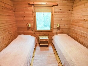Een knus kamer in een chalet, met twee eenpersoonsbedden, een klein houten nachtkastje en een raam met uitzicht op een bos.