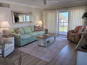 A living room with a sofa, armchair, coffee table, and a large window with curtains.