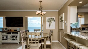 A dining area with a round table and chairs, a TV on the left, and a kitchen area with a bar counter to the right.