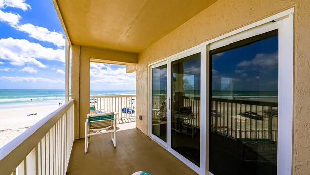 A balcony with a view of the beach, a chair, and a table.