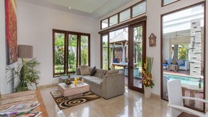 Ein großzügiges Wohnzimmer mit einer großen Couch, einem Couchtisch und einem Essbereich mit einem Holztisch. Große Fenster bieten Blick auf einen Pool im Freien.