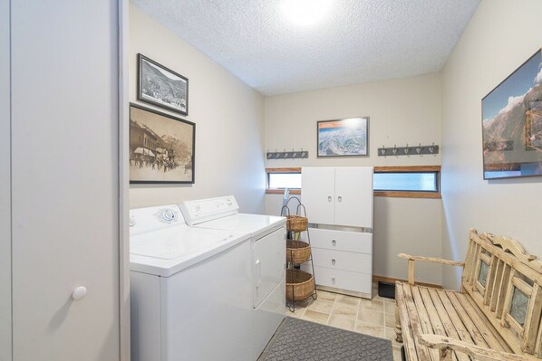 A laundry room with a washing machine, drying rack, and wooden bench.