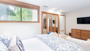 Ett sovrum med en stor säng, en byrå, en tv som är monterad på väggen och en garderob med en spegel.