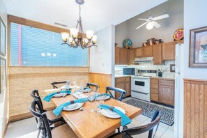 Un coin repas avec une table en bois dressée pour quatre personnes, entourée de chaises, et un lustre au-dessus.