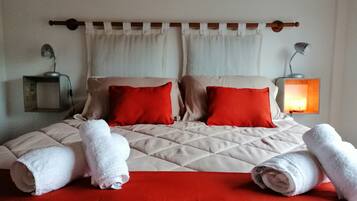A neatly made bed with a red and beige bedspread, two red pillows, and two rolled white towels.