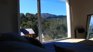 Un dormitorio con un amplio ventanal que ofrece vistas a un área boscosa y montañas.