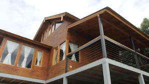 Una cabaña de madera de dos pisos con ventanas amplias y un balcón.