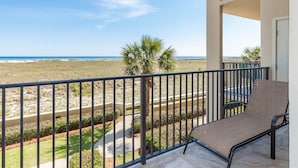 A balcony with a view of the beach, a chair, and a railing.