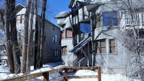Un immeuble résidentiel à plusieurs étages, doté d’un balcon au deuxième étage, d’un escalier en bois et d’un sol recouvert de neige.