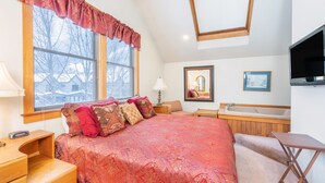 A bedroom with a large bed, a window with a view of trees, a wooden desk, a chair, a bedside table, a lamp, a mirror, a framed picture, and a bathtub. - 1 Block to Lift 7 | Walk to Downtown Telluride | Views, Hot Tub, Parking (Telluride)