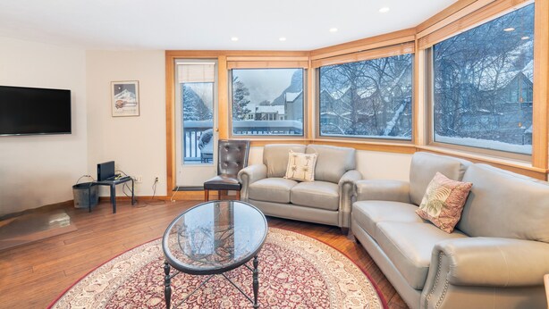 A modern living room with a sofa, a glass coffee table, and a TV mounted on the wall. - 1 Block to Lift 7 | Walk to Downtown Telluride | Views, Hot Tub, Parking (Telluride)