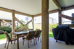 Eine überdachte Terrasse mit Tisch und Stühlen, einem Grill und Blick auf benachbarte Häuser.
